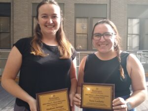 Two graduate students holding plaques